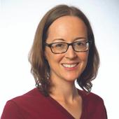 Woman in a red jumper with brown shoulder-length hair and glasses, smiling at the camera