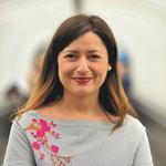 Image of a lady with brown shoulder-length hair in a grey top with flowers on 