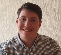 Man with brown hair smiling at the camera. He is wearing a check shirt
