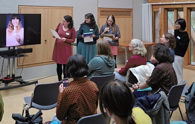 A group of translators are listening to a presentation by 3 presenters who are pointing at an image on a screen
