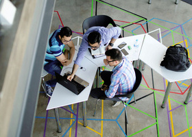A group of people working together at a desk in front of a laptop