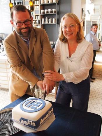 Iwan and Sarah leaning over a table with a knife cutting the blue and white anniversary cake