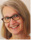Picture of a woman with short blonde hair and glasses smiling at the camera. Her head is tilted to the side 