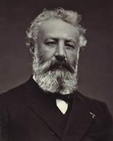 Black and white image of Jules Verne. He has a grey beard and hair, and is wearing a suit jacket and bow tie