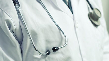 Close-up of a medical stethoscope with black earpieces and silver tubing draped around the neck of a healthcare professional wearing a white coat 