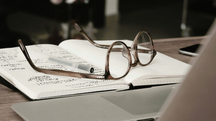 A pair of brown-rimmed eyeglasses rests on an open notebook filled with handwritten notes. 
