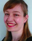 Woman at a 45 degree angle smiling at the camera. She is wearing red lipstick and has ginger hair