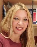 Image of a woman with long blonde hair smiling at the camera in front of a shelf of books.