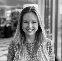 Black and white photo of a lady with long brown hair, wearing a patterned top, smiling 