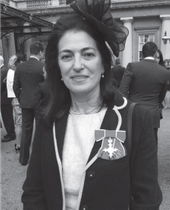 Black and white image of a woman in very smart dress, wearing a fascinator, smiling at the camera. 
