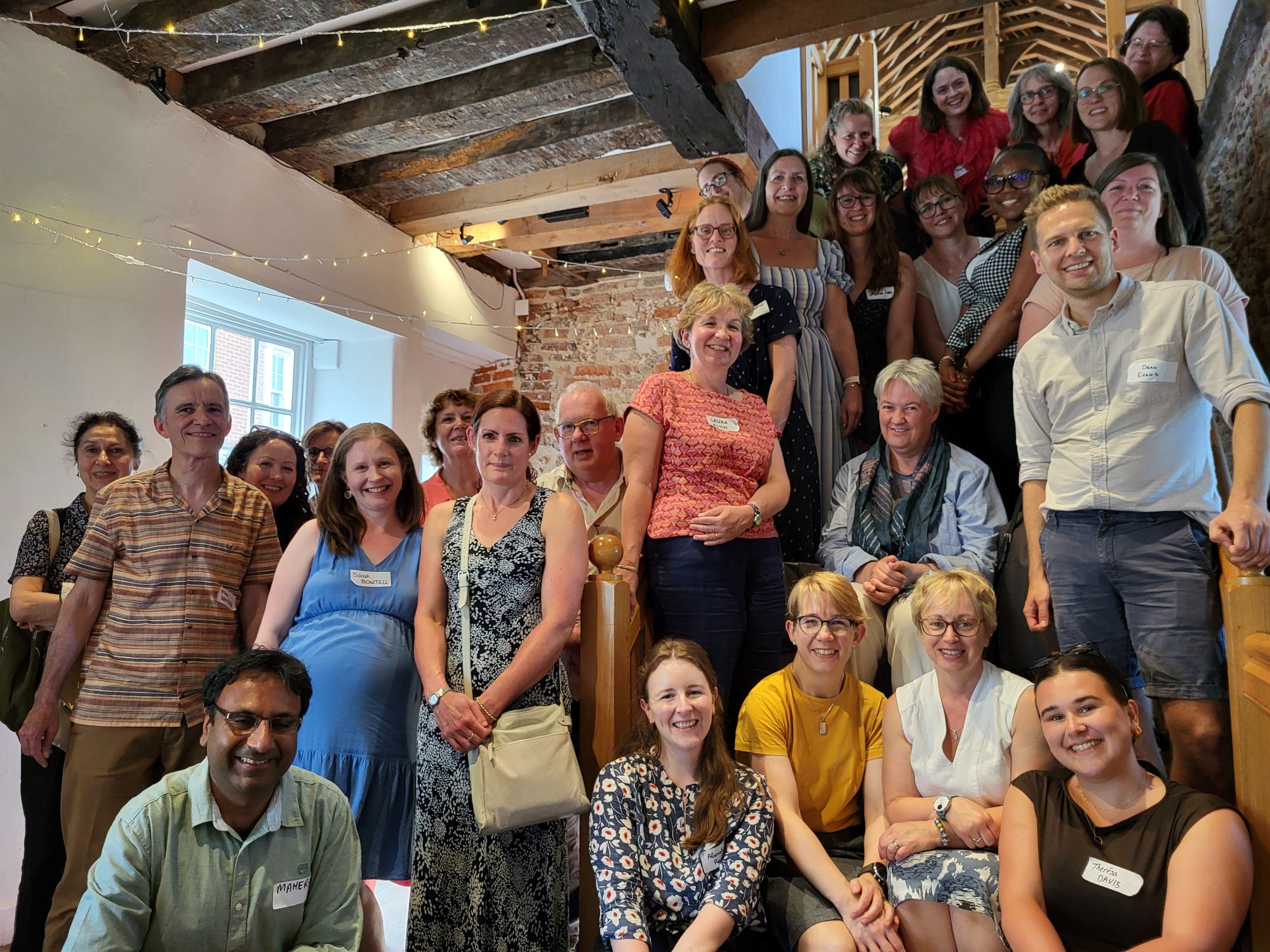 A large group photo of approximately 30 people at what appears to be a professional networking event or conference, gathered on and around a staircase
