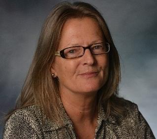 Lady with blond shoulder-length hair and glasses, looking at the camera. She is wearing an animal print shirt 