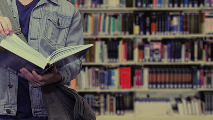Person holding a book open in front of a bookcase