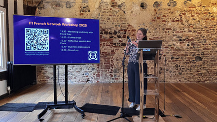 A woman presenting at the ITI French Network Workshop 2025 in a historic venue with exposed stone walls and wooden beams