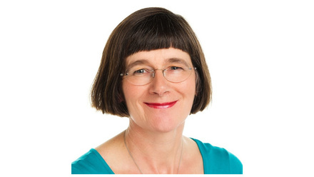 Woman with a black bob and glasses smiling at the camera. She is wearing a teal blue top 