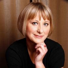 Lady with a blonde bob, resting her chin on her hand, smiling at the camera.