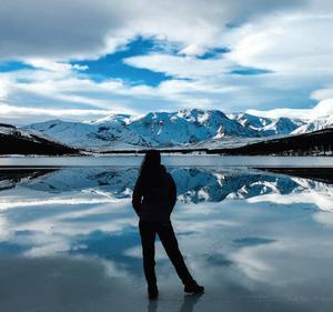 Person standing in front of a mountain landscape, in a cloudy blue sky