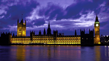 Night view of the illuminated Palace of Westminster in London, including Big Ben, reflected in the River Thames under a dramatic twilight sky