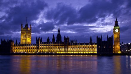 Night view of the illuminated Palace of Westminster in London, including Big Ben, reflected in the River Thames under a dramatic twilight sky