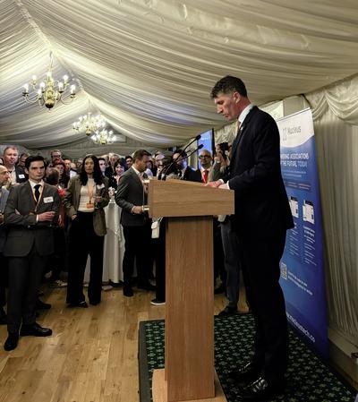 A group of people are listening to a man on a stage giving a welcome speech
