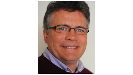 Middle-aged man with grey hair and glasses, smiling