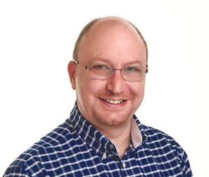Smiling man with glasses, wearing a blue and white checkered shirt, posing against a plain white background