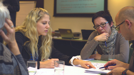 Four people around a table, working together on a document. They look pensive and thoughtful 