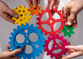 An image of hands holding different coloured and sized cogs, fitted together 