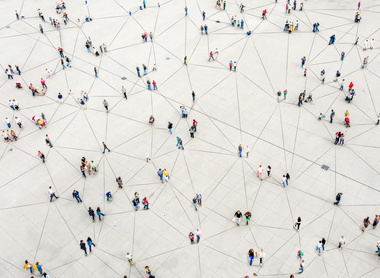 This aerial view shows dozens of people scattered across a large white plaza or public space, appearing as small figures from above.