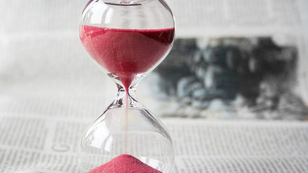 Sand timer with pink sand halfway through, resting on newspaper 