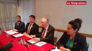 Image of four people - three men and a woman - at a press conference. 