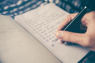 A close-up of someone's hand holding a pen or pencil while writing in an open notebook or journal
